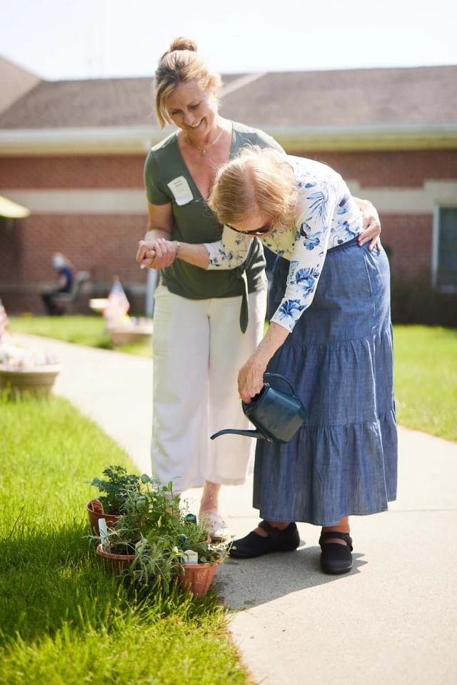 Caregiver helping senior woman water plants