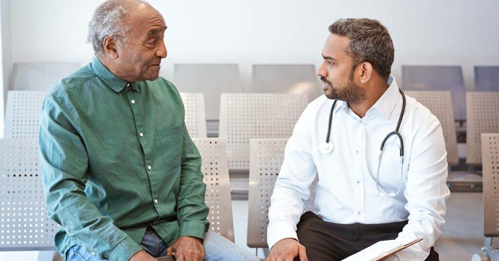 An elderly man sits and talks with his doctor