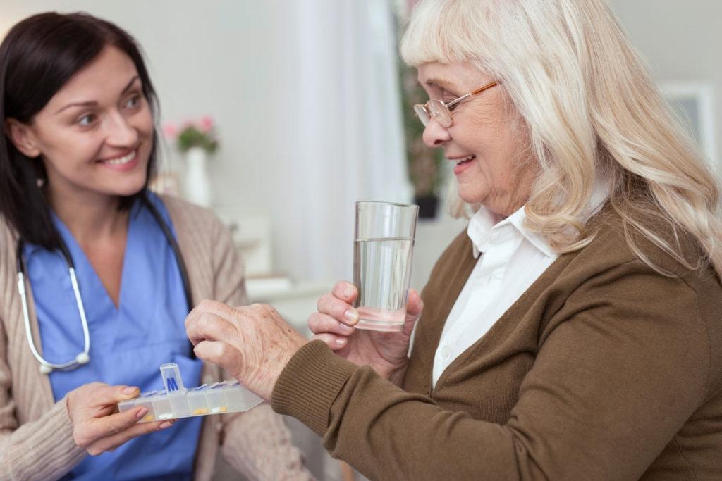 A senior woman taking pills from a pillbox with the help of an assisted living staff