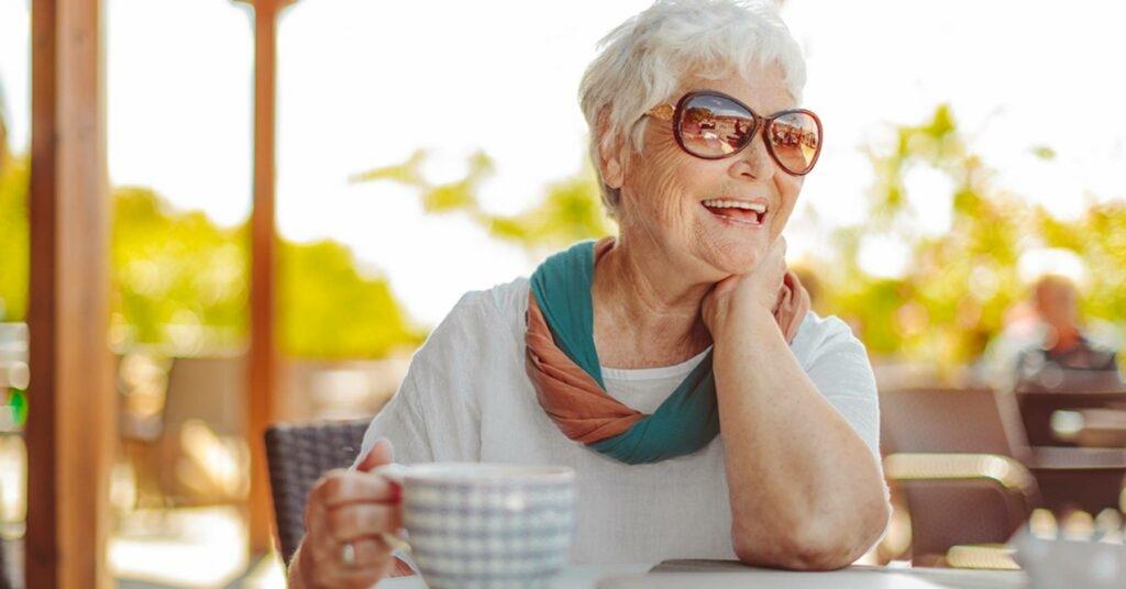 A senior woman smiles while holding a cup of coffee