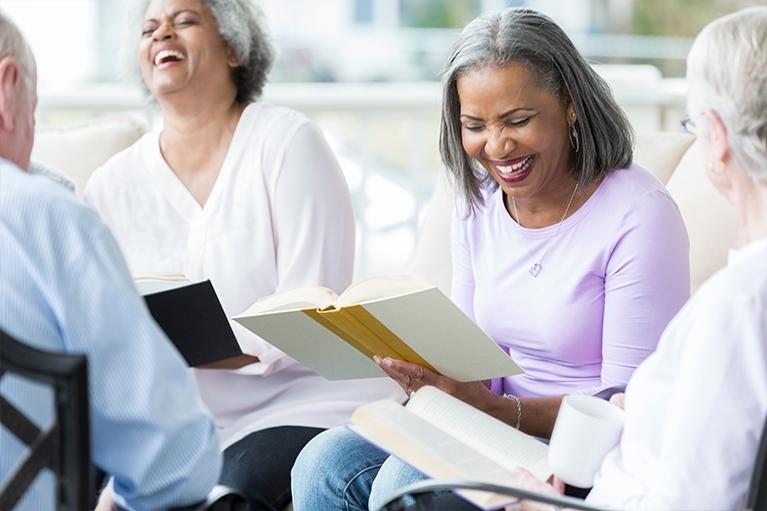 A group of seniors laugh while reading a book together in a book club