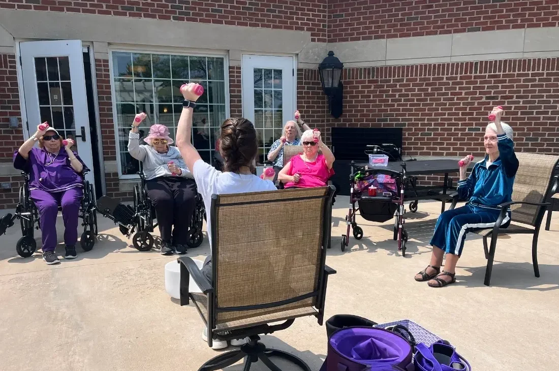 Memory care residents at Ridge Crest at Meadow Ridge participate in an outdoor exercise class, lifting small hand weights together under the guidance of an instructor.