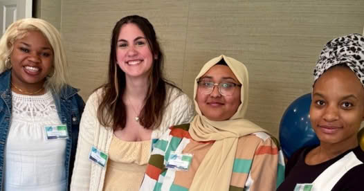 Four smiling Meadow Ridge associates stand together indoors at a scholarship celebration, wearing name badges and casual attire, representing the impact of Country Store proceeds and resident generosity supporting the Meadow Ridge Scholarship Fund.